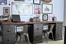 a double vintage industrial desk of metal and wood, with metal chairs and a large and bright gallery wall over it