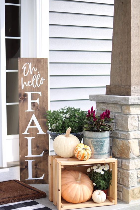 a fall sign, some fall blooms and plants, natural pumpkins in and on a crate for a Thanksgiving porch