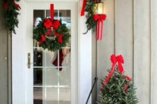a farmhouse Christmas porch with an evergreen garland with red bows and a matching wreath plus a tree with lights and gift boxes