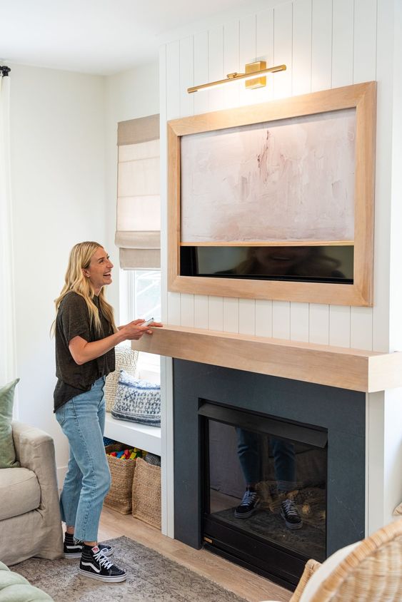 a farmhouse space with a fireplace, a TV on the wall and an artwork hiding the TV is a cool idea