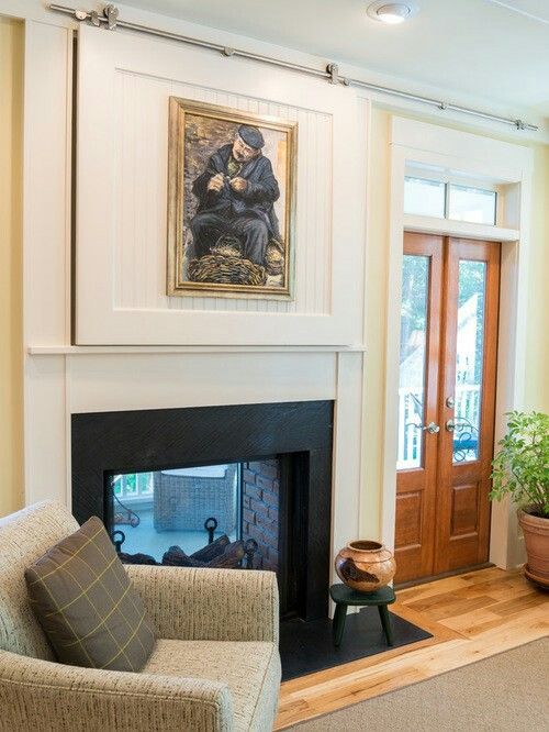 a fireplace and a TV over it hidden with a sliding door featuring an artwork are a traditional solution for a modern space