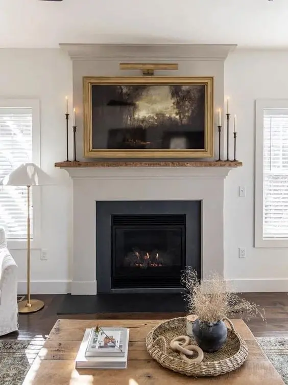 a fireplace and a framed TV over it, in a chic gilded frame, is a beautiful way to hide a TV right in sight and do it with style
