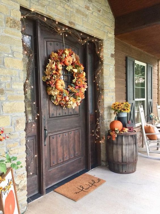 a front door highlighted with lights, a lush wreath of pumpkins and leaves, some pumpkins and leaves next to it