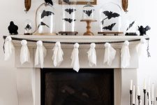 a fun Halloween mantel decorated with black bats in cloches and a garland of white ghosts is a cool idea for a holiday