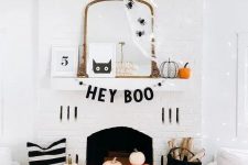 a fun modern Halloween fireplace with a letter banner, signs, pumpkins, firewood and a cat artwork plus some spiders on the mirror