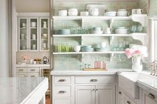 a glam cottage kitchen with white shaker cabinets, stone countertops and open shelves, a green tile backsplash and chic porcelain
