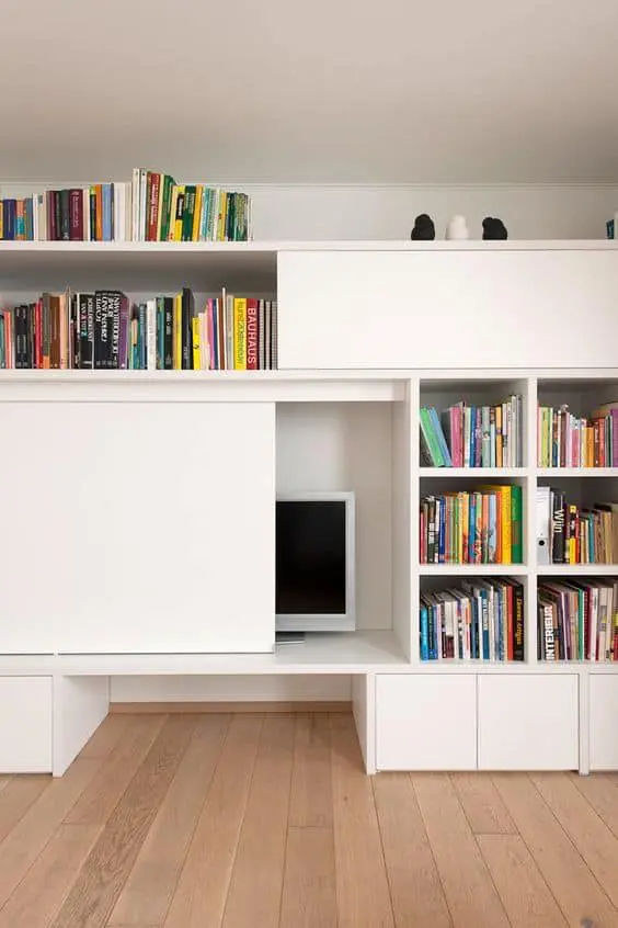 a large white storage unit with bookshelves and a TV hidden with a sliding door is a cool and smart solution