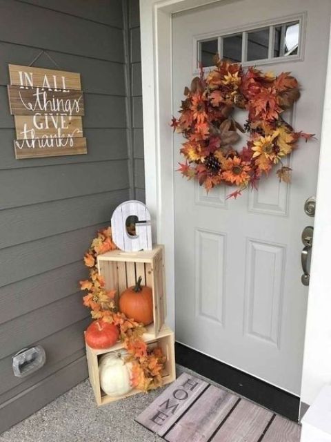 a lush fall leaf and bloom wreath with pinecones, crates with fall leaves and pumpkins for a Thanksgiving porch