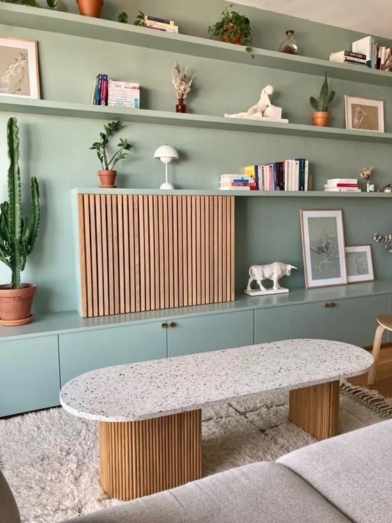 a mint green wall with matching shelves and storage cbainets, a TV hidden with a fluted piece that looks very cohesive here