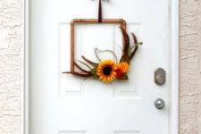 a modern copper pipe wreath with feathers, fall blooms and a brown ribbon for a chic look