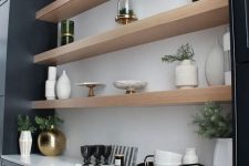 a modern farmhouse home bar with black shaker style cabinets, open shelves, brass conces and potted greenery