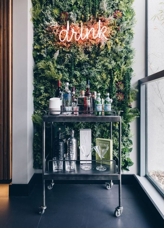 a modern home bar space with a green wall, a neon light and a metal cart with various drinks is very bold