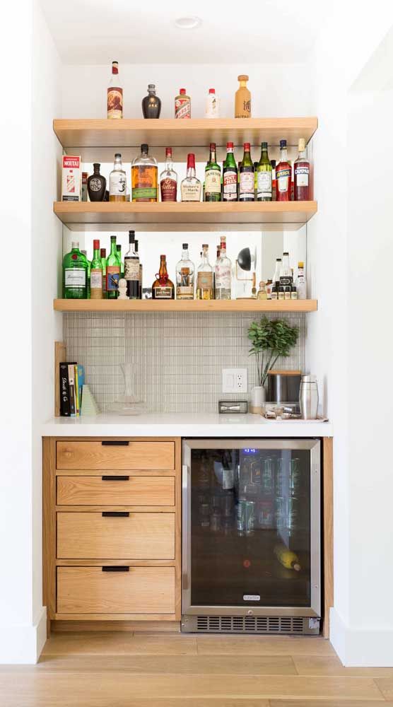 a neutral built-in home bar with open shelves, a mirror, drawers and a wine cooler, with potted greenery and books