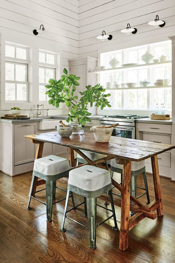 a neutral cottage kitchen with planked walls, white vintage cabinets, open shelves, sconces, a stained table and metal stools