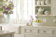 a pastel cottage kitchen with light green shaker cabinets, a beadboard backsplash, open shelves and neutral stone countertops