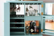 a pretty turquoise cabinet with mirrors inside, with wine bottles and glasses, blooms, a tray with wine and wine glasses
