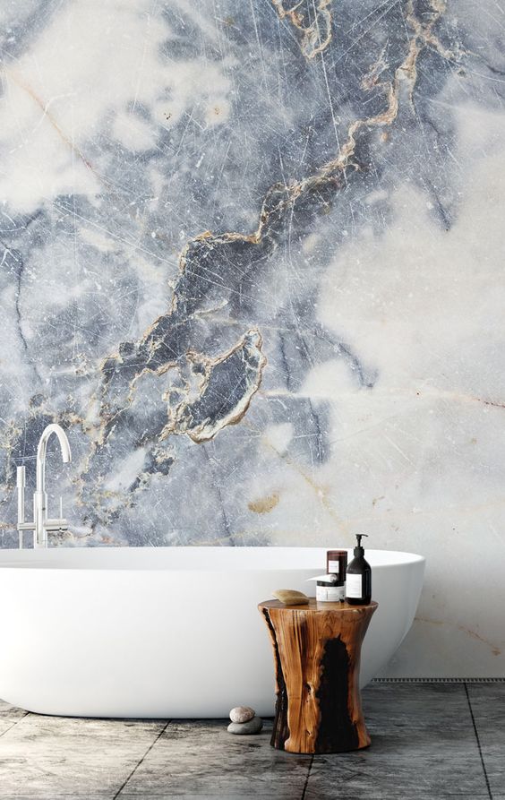 A refined bathroom with a fantastic marble wall, a free standin bathtub and a tree stump stool or side table