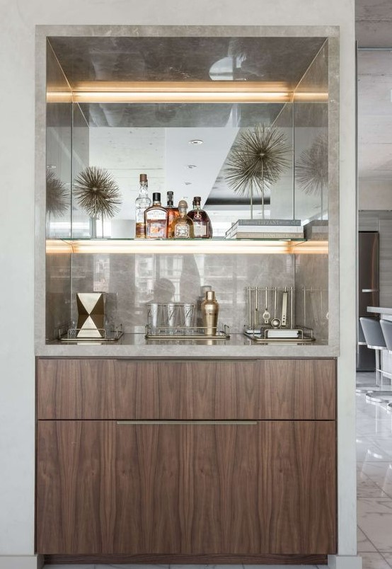 A refined built in home bar with neutral marble, lit up shelves and sleek drawers is very chic and stylish