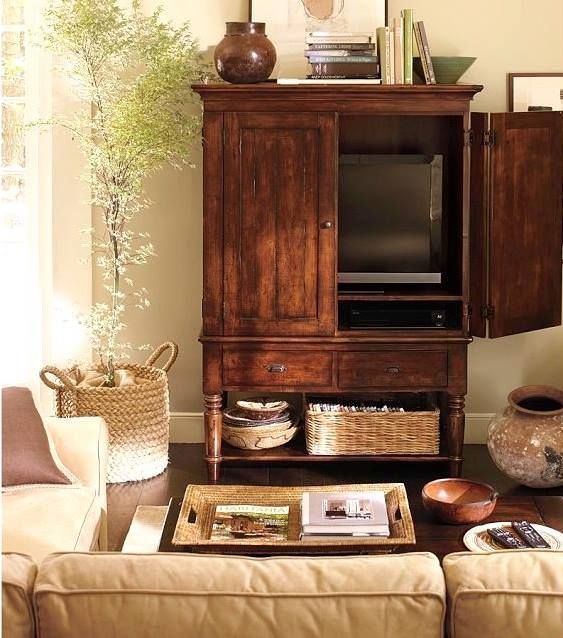 A rich stained storage unit with a TV hidden inside, baskets and books in it is a perfect solution for a rustic space