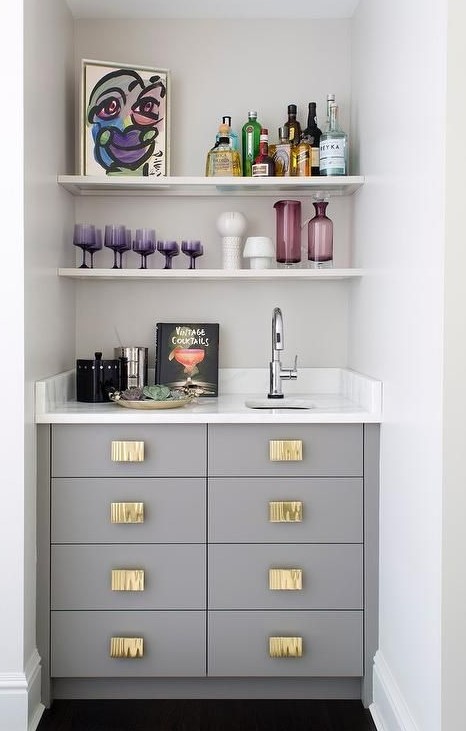 A small yet chic built in bar with a sink, open shelves, drawers and a marble countertop plus colorful glass