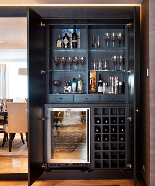A sophisticated and beautiful built in home bar of dark stained wood, with a wine cooler, open storage compartments and glass shelves