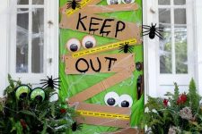 a super bold and catchy front door in green, with signs, googly eyes, spiders is a very fun and colorful idea for Halloween
