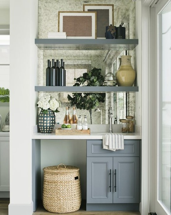 A tiny built in home bar with a mirror backsplash, open shelves, a cabinet and a sink plus blooms and a basket