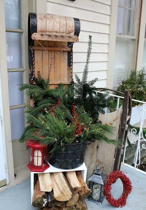 a vintage sleigh, a bucket with fir branches and berries, firewood, a red lantern,a berry wreath for a cozy rustic feel