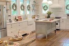 a welcoming cottage kitchen with white planked walls, shaker style cabinets, a shabby chic kitchen island, pendant lamps hanging from a reclaimed wooden ceiling