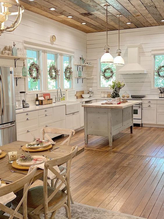 a welcoming cottage kitchen with white planked walls, shaker style cabinets, a shabby chic kitchen island, pendant lamps hanging from a reclaimed wooden ceiling
