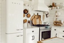 a white cottage kitchen with planked walls and a hood, white shaker cabinets, cool appliances, a stained kitchen island and lots of wood items for decor and usage