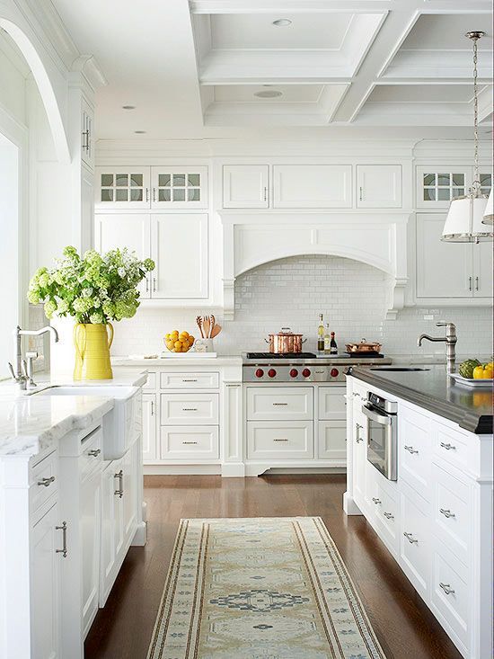 an enchanting cottage kitchen with white shaker cabinets, a coffered ceiling, a large kitchen island with a contrasting countertop and greenery
