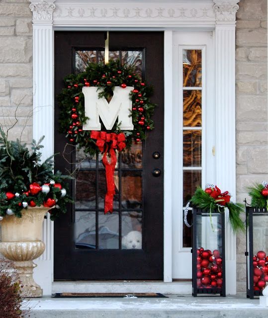 an evergreen wreath with red ornaments, a red bow, a monogram and candles with red ornaments inside