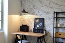 an industrial home office with white brick walls, a trestle desk of wood and metal, a pretty chair and pendant lamps