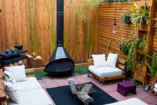 an outdoor space with white seating furniture, a black Malm fireplace, a black rug, purple stools and potted greenery