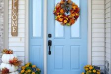 bold fall blooms in pots, white pumpkins stacked with fall leaves, a wreath fo fall leaves and with a bow