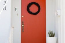 bright pumpkins and a black wreath on the orange door are perfect to style your modern front porch for Halloween
