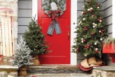 cozy Christmas front door decor with an evergreen garland, mini trees and a large one with red and white ornaments plus a snowy wreath