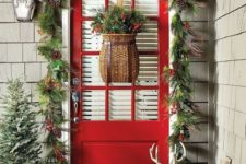 cozy rustic Christmas front door styling with an evergreen garland with berries and pinecones, a snowy mini tree and red boots