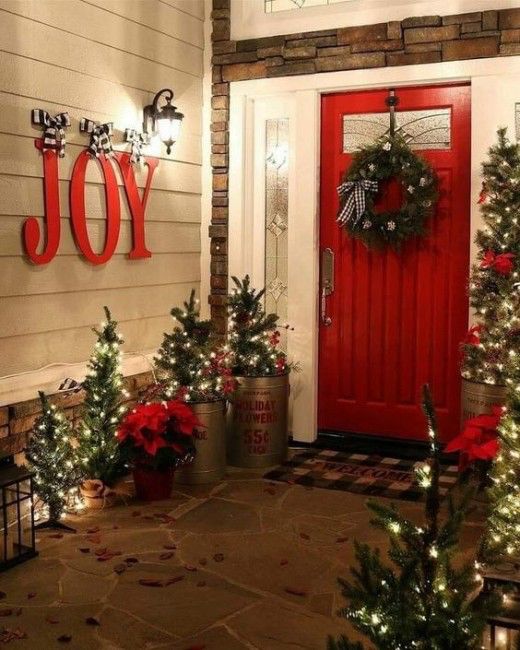 lots of mini Christmas trees with lights, JOY letters, a wreath and red touches for a lovely rustic front porch