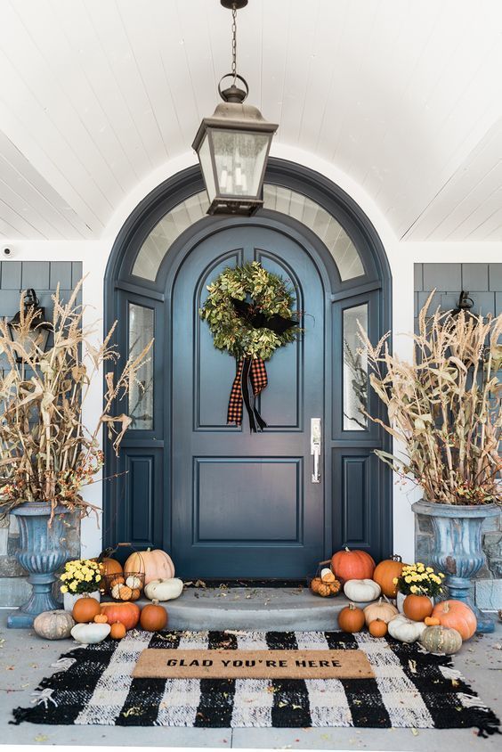 lots of natural pumpkins on the floor, corn husks in vintage urns and a greenery wreath with plaid ribbons in the door