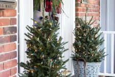mini Christmas trees in buckets with lights, a fir branch hanging with a plaid scarf make the porch look rustic and cozy