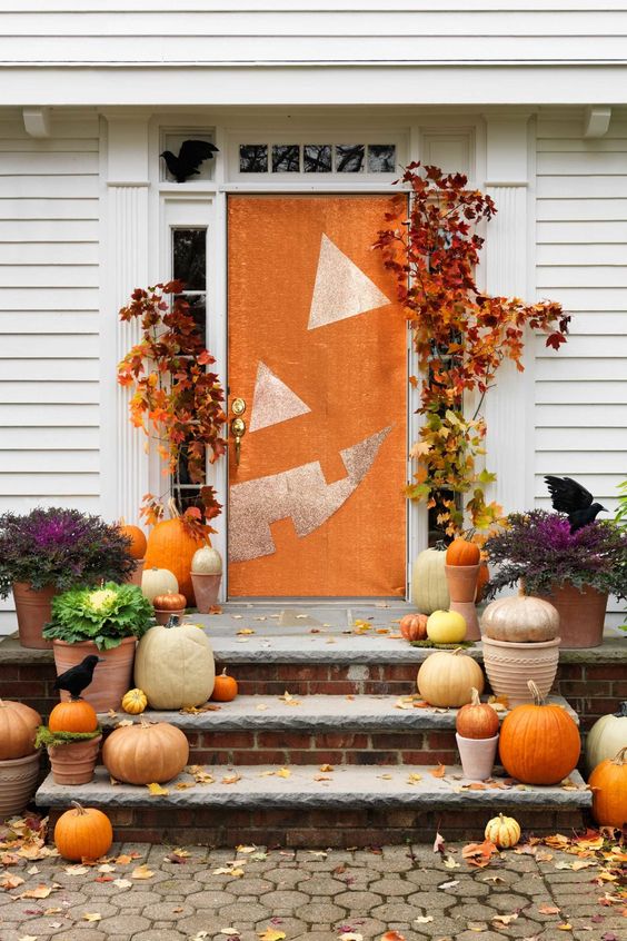 Natural pumpkins, spray painted or not, fall leaves and a front door styled as a jack o lantern for a bright Halloween porch
