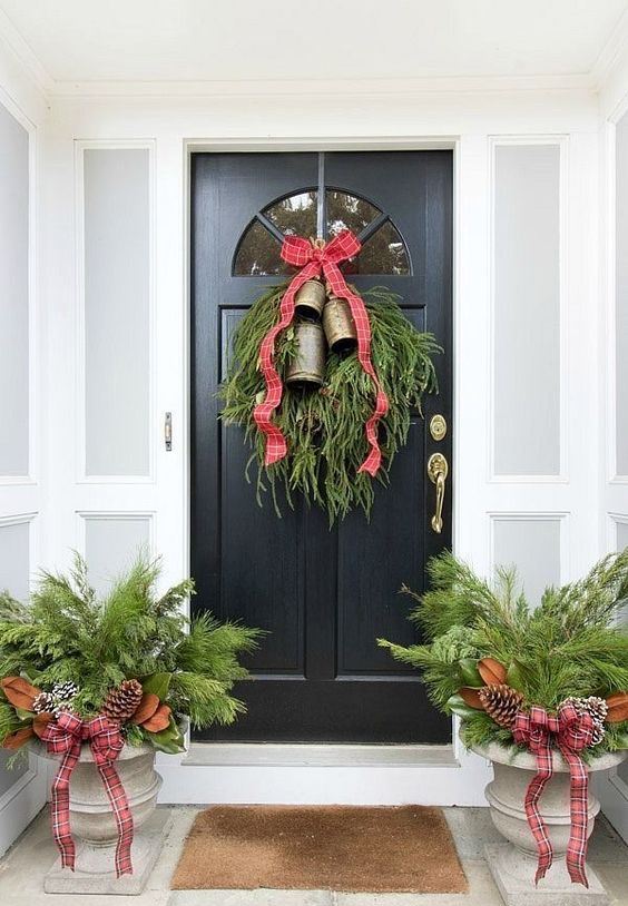 rustic Christmas front door styling with large bells, evergreens, snowy pinecones and magnolia leaves plus plaid ribbons