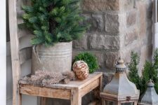 rustic vintage porch decor with oversized pinecones, greenery balls and a mini tree in a bucket plus wooden candle lanterns