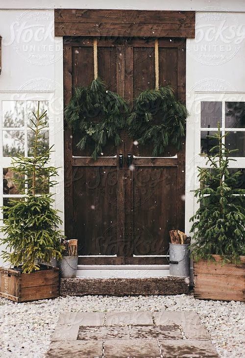 simple rustic front porch decor with Christmas trees in crates, buckets with firewood, fir wreaths on ribbons looks al-natural