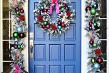super bright Christmas front door decor with a silver garland with colorful ornaments, striped bows and  a matching wreath plus colorfil gift boxes