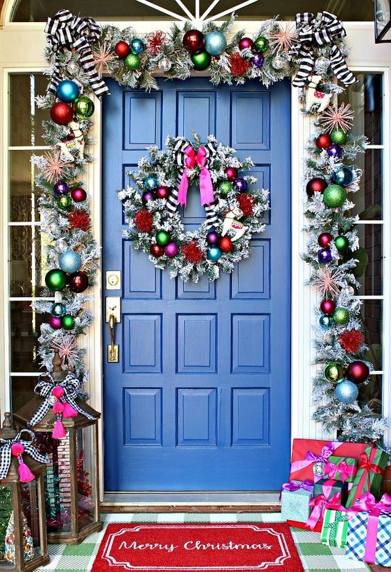 super bright Christmas front door decor with a silver garland with colorful ornaments, striped bows and  a matching wreath plus colorfil gift boxes
