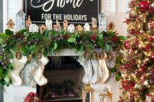 a Christmas mantel with an evergreen and snowy pinecone garland, mini houses and stockings plus a Christmas sign with matching decor