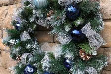 a Christmas wreath with bold blue and light blue ornaments, pinecones and silver ribbons is a lovely and chic idea